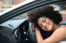 Portrait of a woman smiling and laying her head on the steering wheel of new car