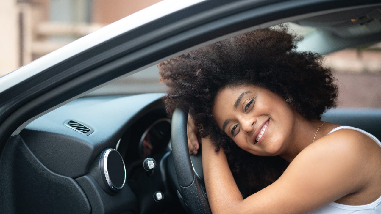 Portrait of a woman smiling and laying her head on the steering wheel of new car