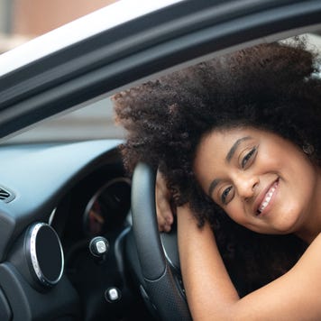 Portrait of a woman smiling and laying her head on the steering wheel of new car