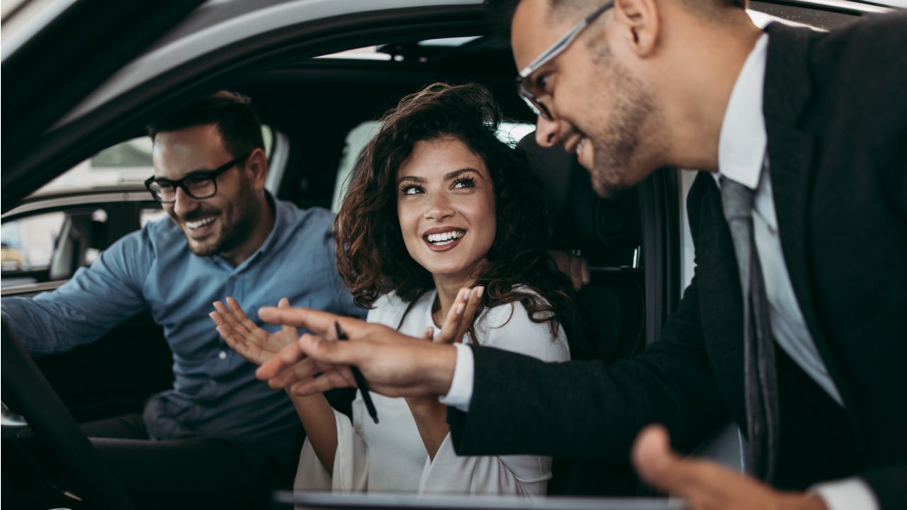 Man and woman sit in a car at a dealership