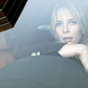 Blonde woman stares out windshield while leaning on steering wheel.