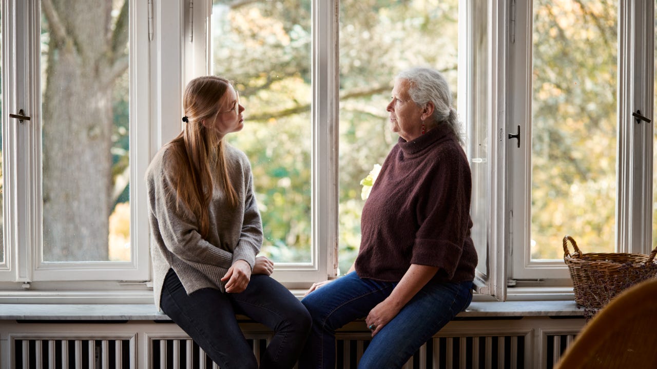 A younger woman and an older woman sitting on a window seat facing one another