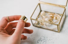 A woman holds a gold ring in front of a jewelry box