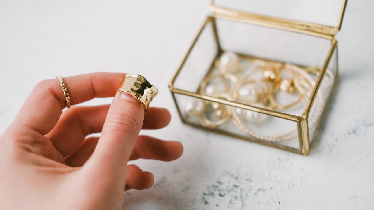 A woman holds a gold ring in front of a jewelry box