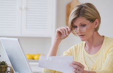 Woman lowering glasses while looking over paper with laptop in front of her