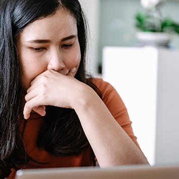 Close up of woman leaning on her hand while looking at laptop