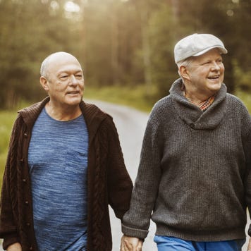An elderly gay couple walks together on a nice, scenic forest road.