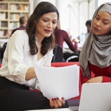 Woman explains paperwork to younger woman in library