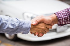 Two pale hands shaking in front of white car