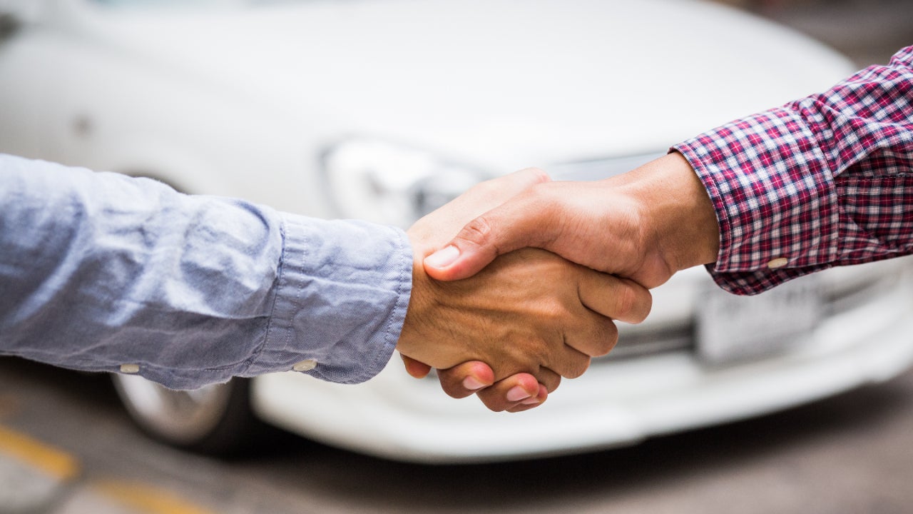 Two pale hands shaking in front of white car