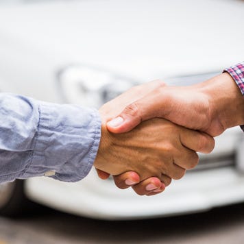 Two pale hands shaking in front of white car