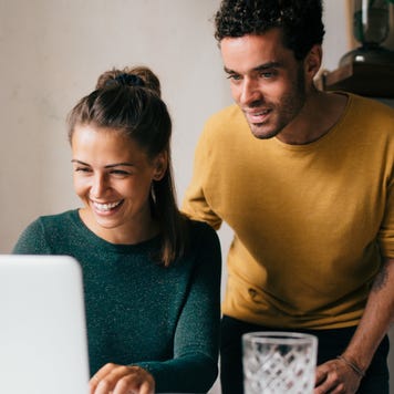 Smiling woman on laptop with curious man looking over her shoulder