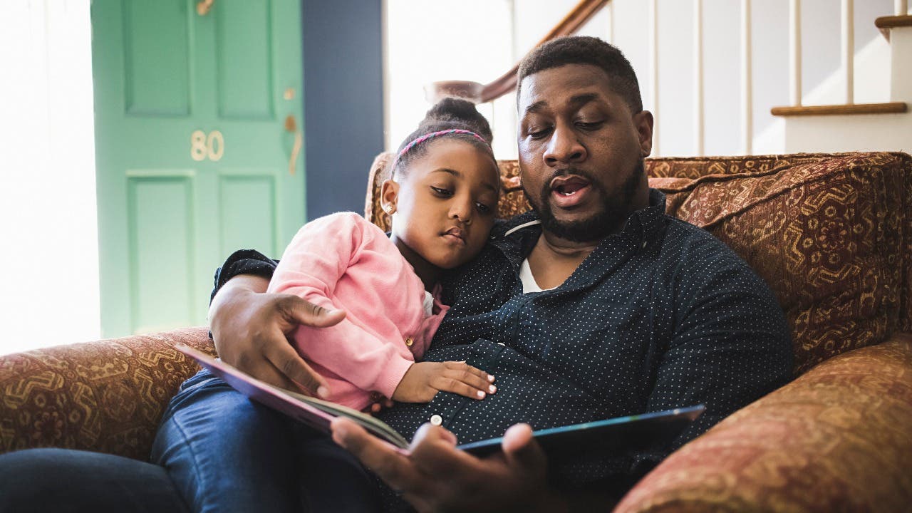 Man reads a book to young daughter