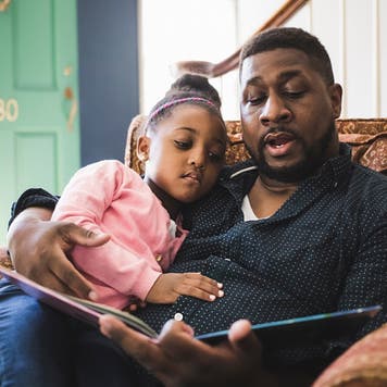 Man reads a book to young daughter