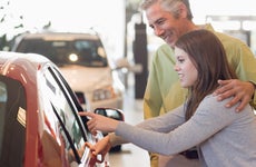 Smiling girl and her father looking at car in showroom, girl pointing at car