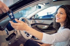 Smiling woman sitting in driver's seat accepting a key from hand off camera