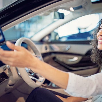 Smiling woman sitting in driver's seat accepting a key from hand off camera