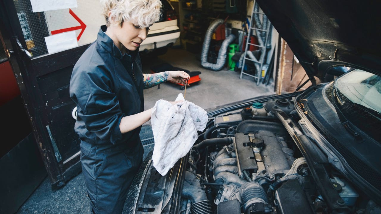 Side view of female mechanic checking oil of car parked outside auto repair shop