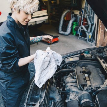 Side view of female mechanic checking oil of car parked outside auto repair shop