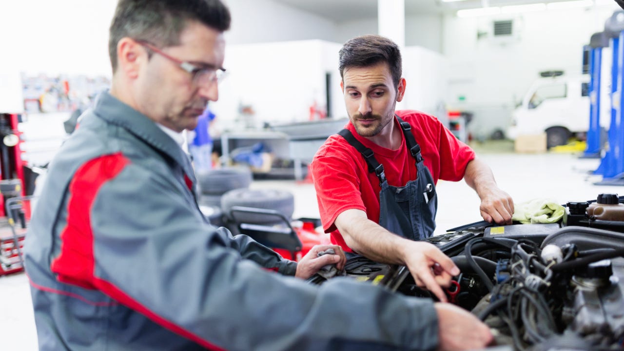 Two men working under an open car hood in a mechanic shop