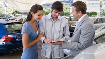 Man and woman standing with car salesperson, signing a document