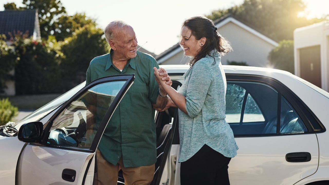 Woman helping older man out of car, both smiling