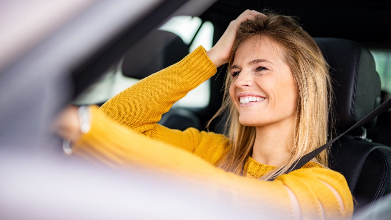 Close up three-quarters view of of smiling woman in driver's seat looking out the windshield