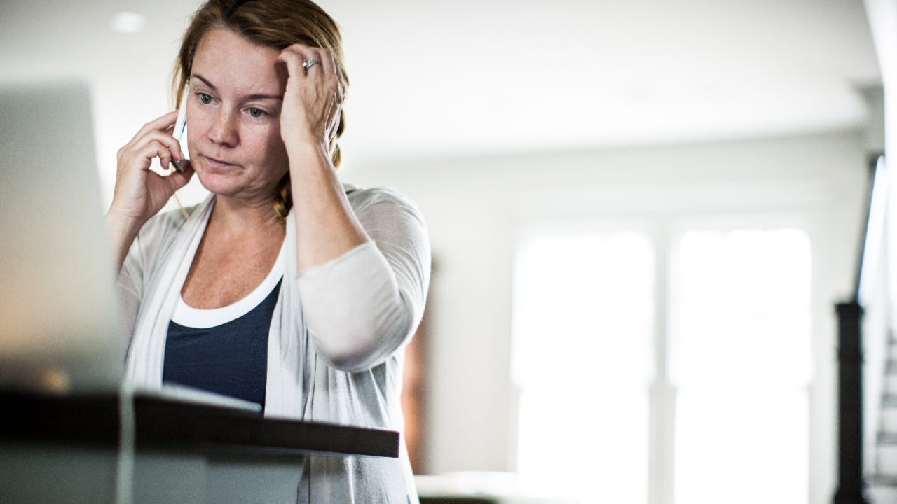 Perplexed woman on phone while looking at laptop