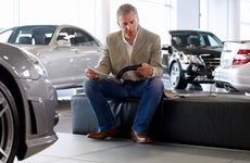 Man sits on low bench in the middle of car showroom looking at brochure