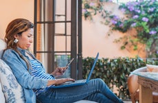 Woman sitting on patio with open laptop on lap and phone in hand