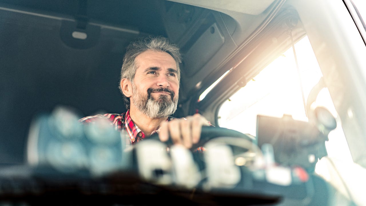 Close up through windshield of happy older man driving truck