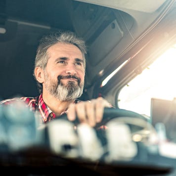 Close up through windshield of happy older man driving truck