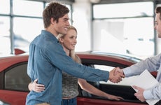 Woman standing next to car with arm around man who is shaking the hand of a car dealer