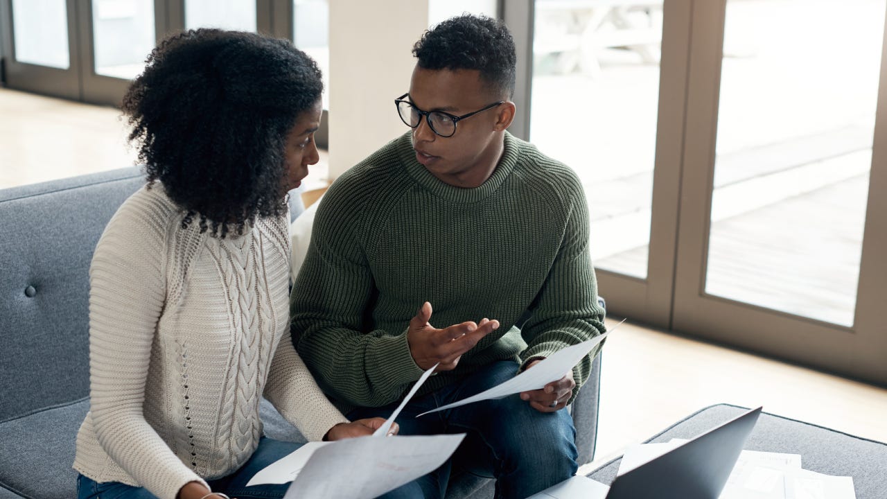 A black couple sits together in the living room reviewing their policy and if they need to switch.