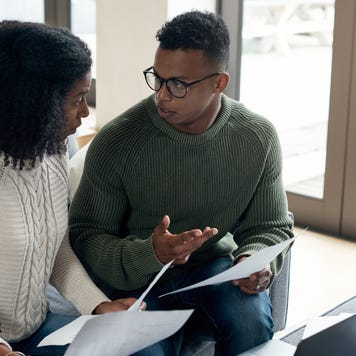 A black couple sits together in the living room reviewing their policy and if they need to switch.