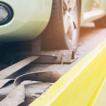Close up of car on tow truck bed with man in background tying car down