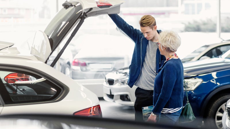 Smiling mother and serious son examining trunk of car in dealership