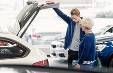 Smiling mother and serious son examining trunk of car in dealership