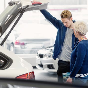 Smiling mother and serious son examining trunk of car in dealership