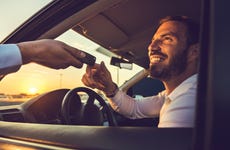 Smiling man sitting in car receives keys through open window.