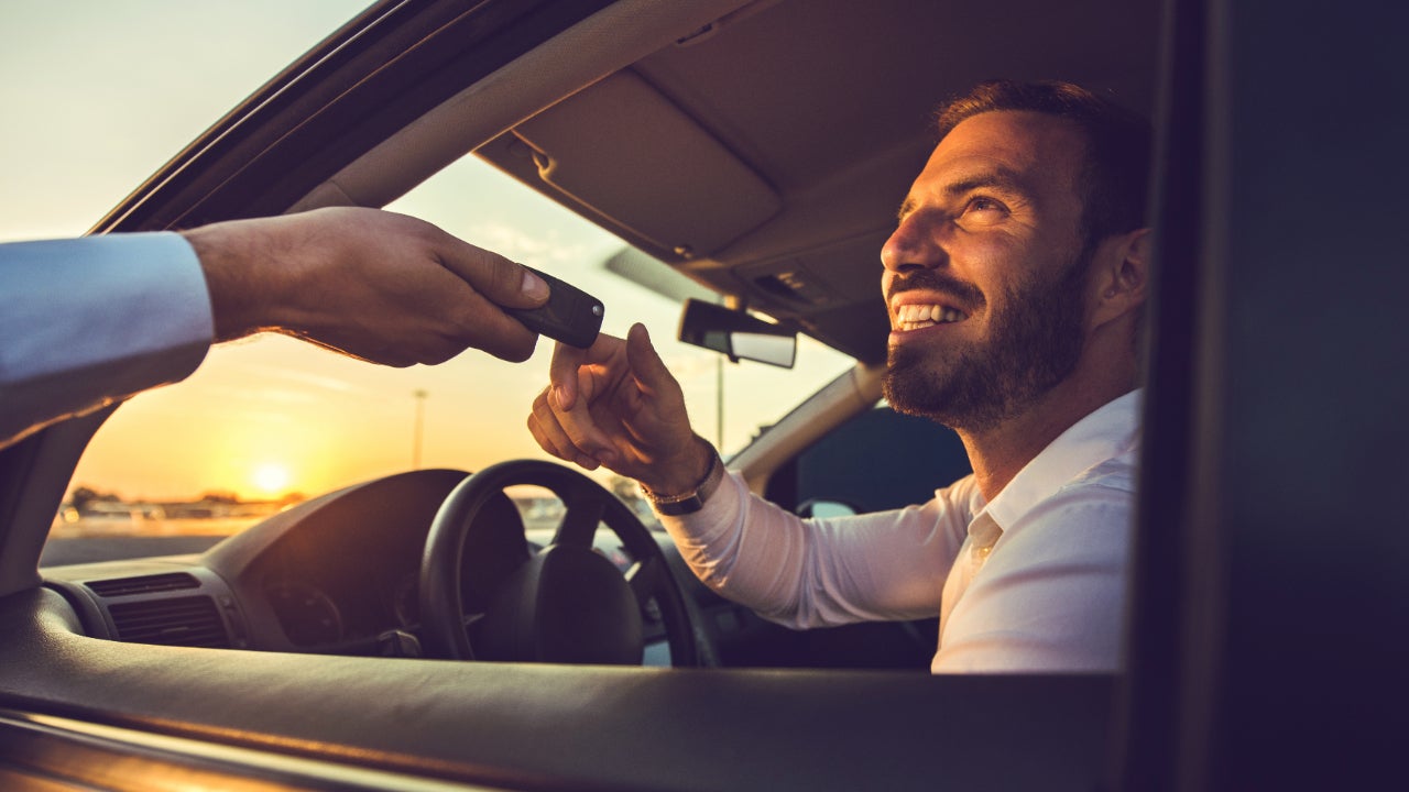 Smiling man sitting in car receives keys through open window.
