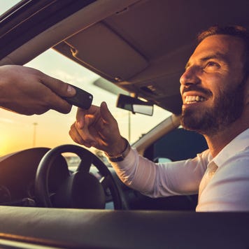 Smiling man sitting in car receives keys through open window.
