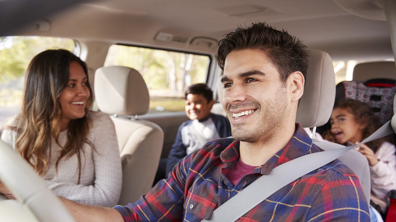 A man drives his family on a trip in their van; everyone is smiling and having a great time!