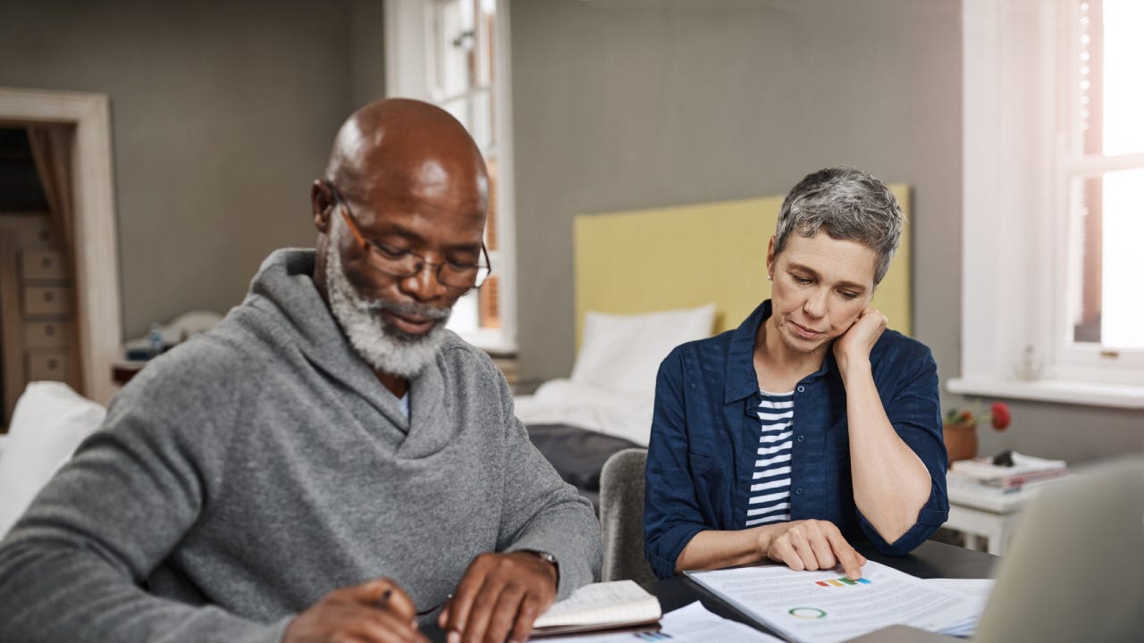 Older interracial couple sitting together at a desk and reviewing their options financially.