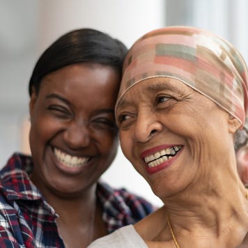 A mother and daughter smile together for a picture. The mother is wearing a silk scarf over hear head as she is undergoing chemotherapy.