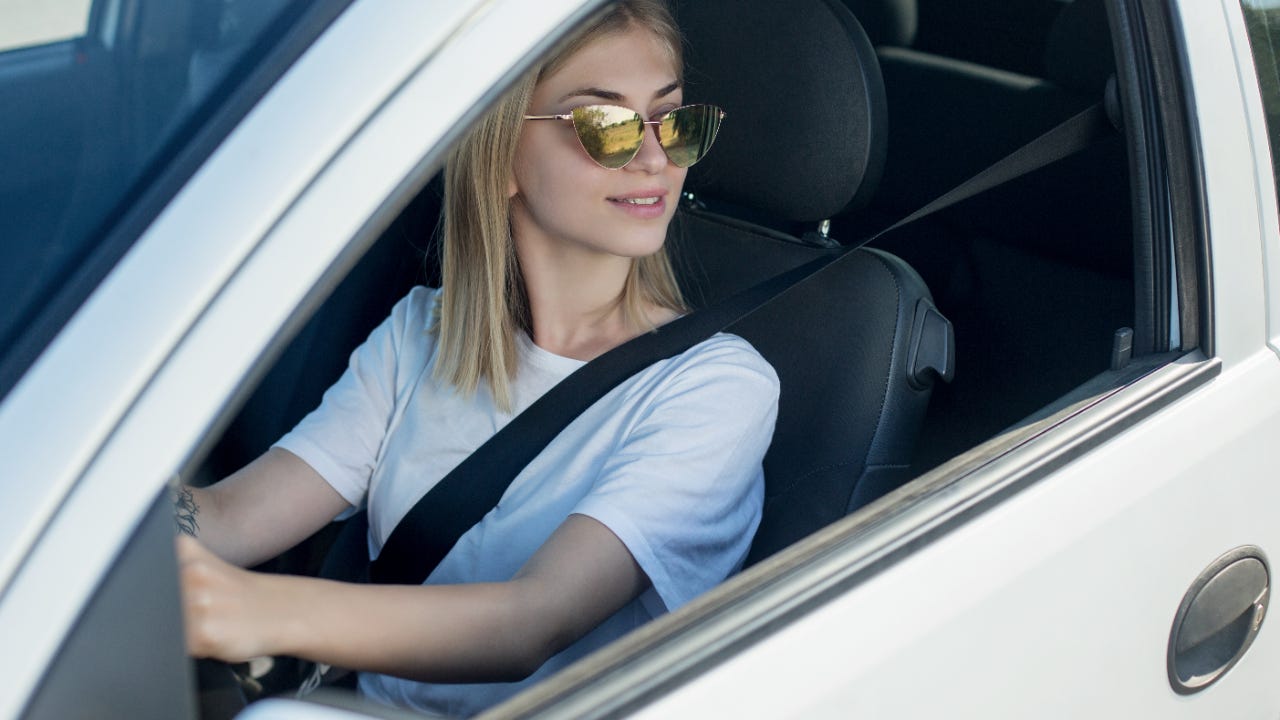 A woman wearing sunglasses looks out an open car window.