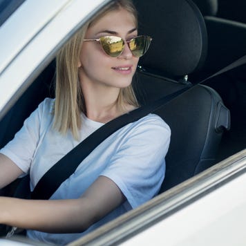 A woman wearing sunglasses looks out an open car window.