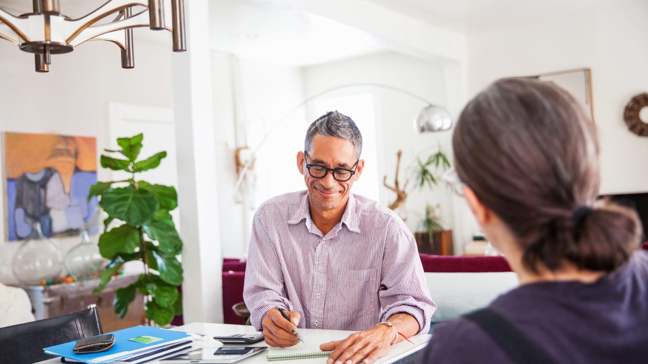 A man wearing glasses sits down at a table with an insurance agent signing a new plan.