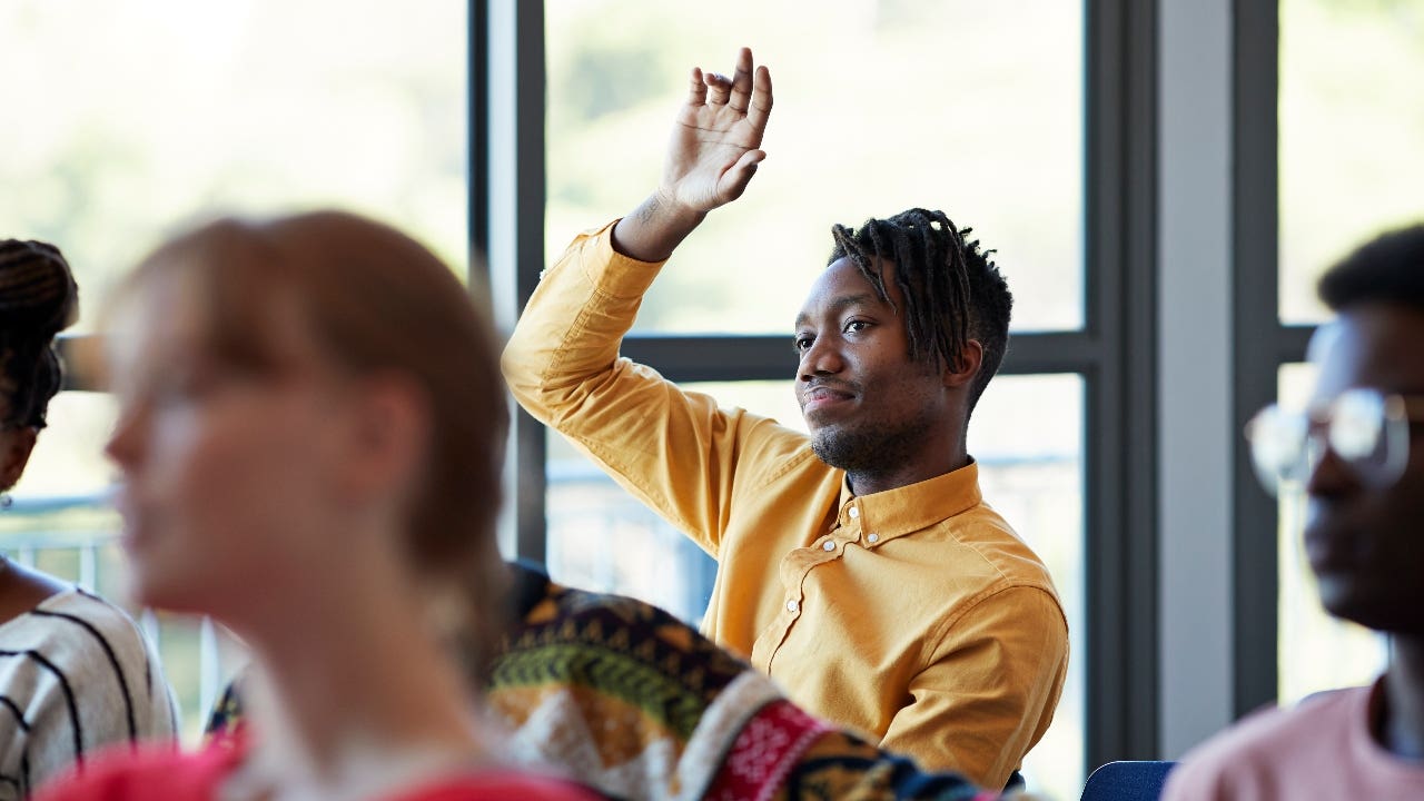 Student raises his hand in college classroom