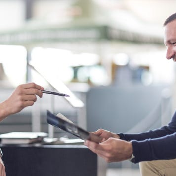 Three people sitting together with a blurred background, one man on the left pointing with a pen and a man and a woman on the right smiling and reviewing a paper